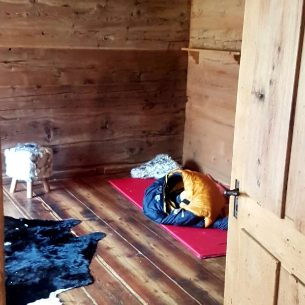 Mein erster Abend im Maiensäss - leeres Wohnzimmer, nur Schlafsack, Teppich und Hocker, ganz ohne Strom