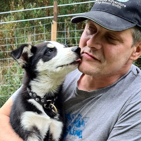 Nahaufnahme von Phil mit Husky-Welpen Jagger im Arm - liebevoller Moment, Jagger schleckt Phils Wange