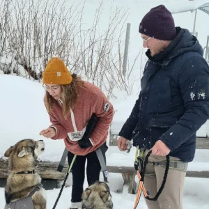 Zwei Gäste beim Wintertrekking in Saas-Fee - Pause im Schnee mit Leckerlis für ihre Huskys